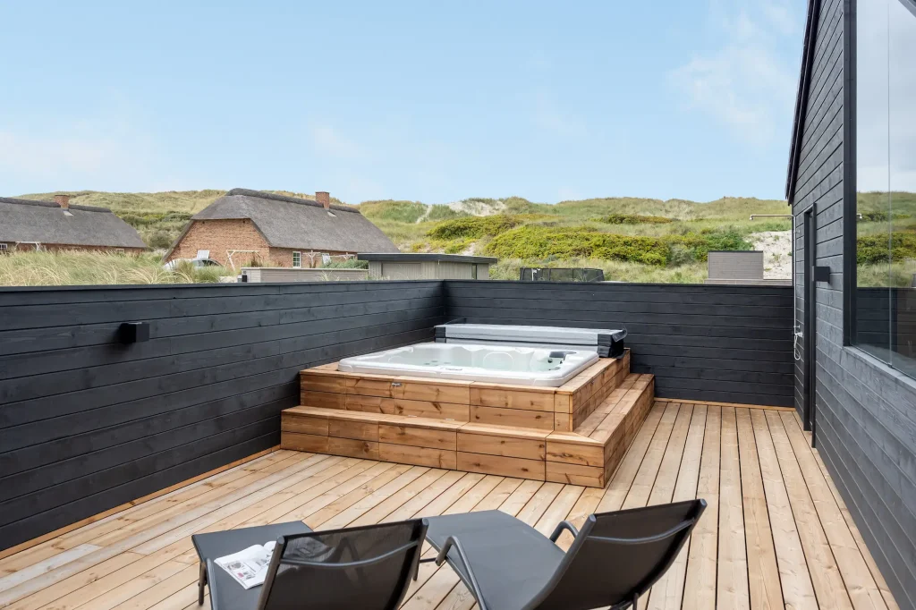 luksus-sommerhus med udespa på træterasse og udsigt til klitter og himmel